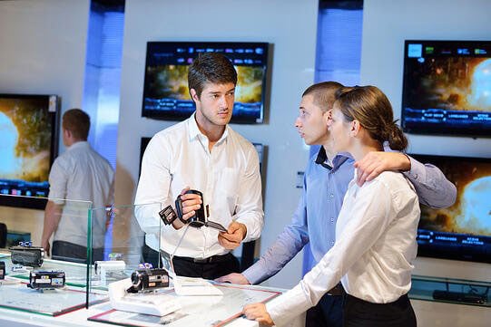 Young couple in consumer electronics store looking at latest laptop, television and photo camera to buy